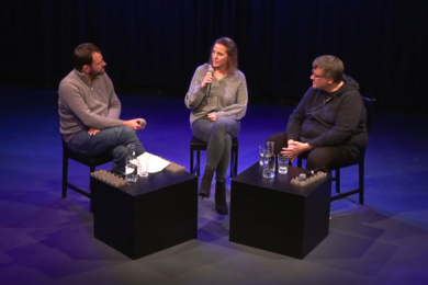 Drei Personen sitzen auf der Bühne und diskutieren